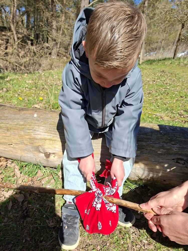 Een jongen knoopt een rood doekje om een stok